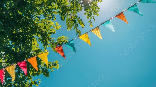 colorful pennant string decoration in green tree foliage on blue sky, summer party background template banner with copy space