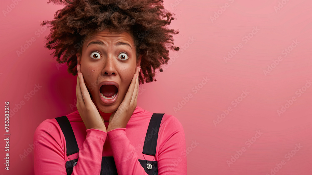 Amazed African American female wearing pink turtleneck and black overall touching face and looking at camera with open mouth surprised with news Amazed African American female wearing pink turtleneck and black overall touching face and looking at camera with open mouth surprised with news