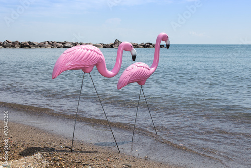 Pink plastic lawn ornament flamingos in a realistic beach setting standing in the water photo