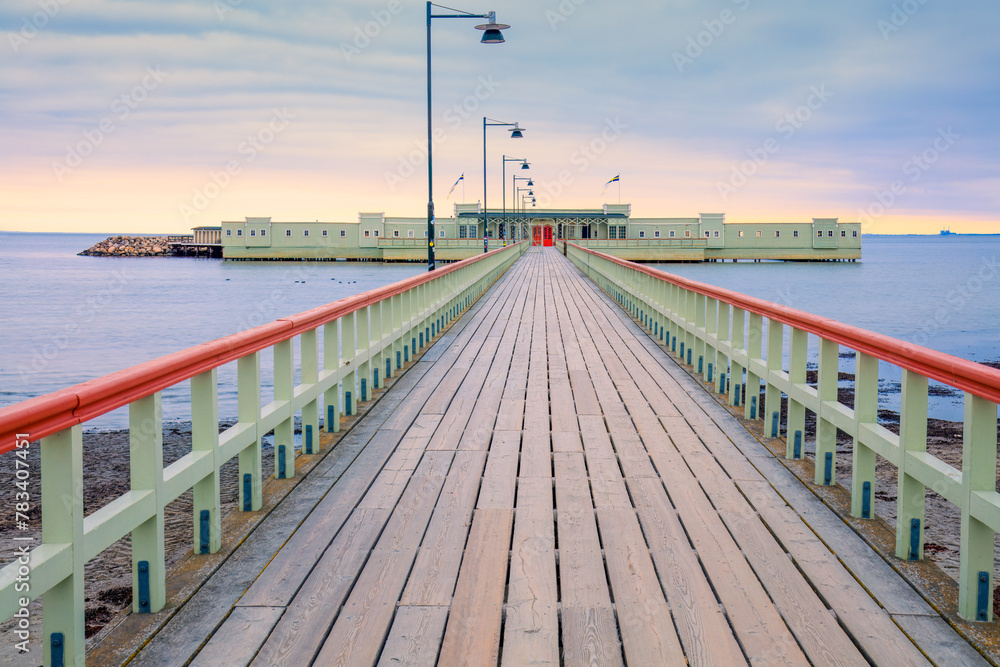 Pastel-colored bathhouse at the end of the wooden pier in dawn. The serene setting evokes peace and a bygone era. Concepts: tranquility, heritage, Malmo