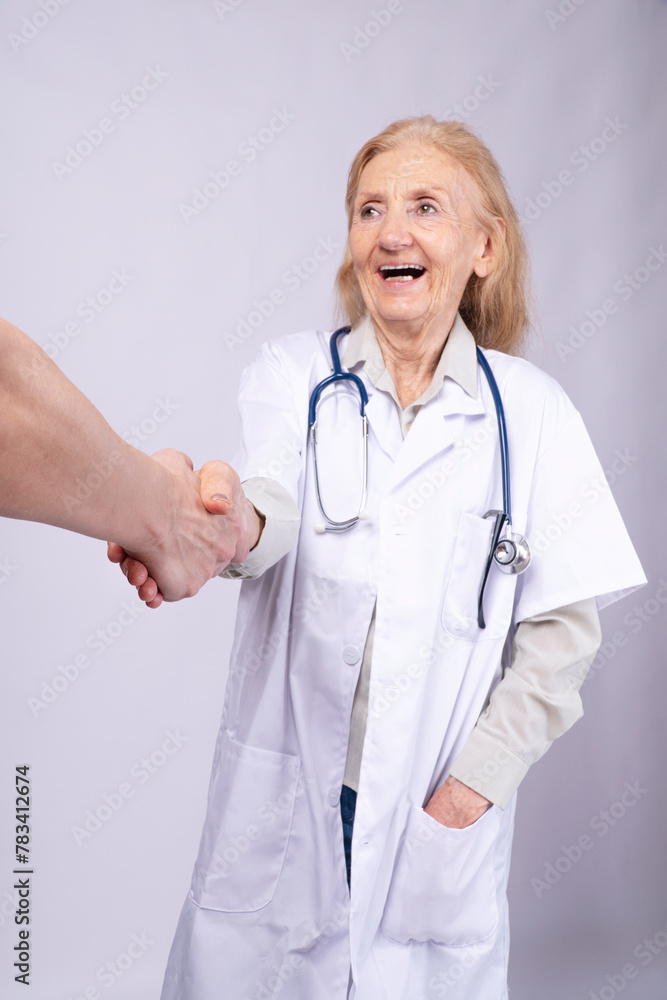 Happy senior doctor woman wear uniform lab coat stethoscope handshake patient standing over white background. Confident elderly doctor career handshake greeting agreement. Health career occupation Happy senior doctor woman wear uniform lab coat stethoscope handshake patient standing over white background. Confident elderly doctor career handshake greeting agreement. Health career occupation