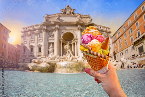 Italian bright sweet ice cream gelato cone with different flavors held in hand on the background of  famous Trevi Fountain in Rome, Italy