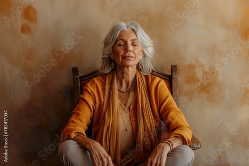 A mature woman sitting in a chair with her eyes closed, showing a meditative posture.