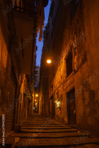 Dark atmospheric alley with stairs illuminated by street lights during blue hour on a winter evening, Naples, Campania, Italy