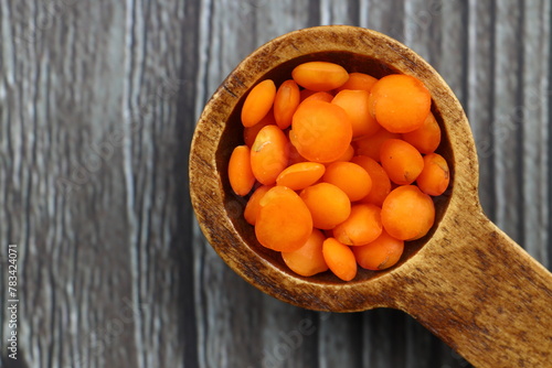 Red lentils in a wooden spoon on an old wooden table close-up. Vegetarian food.
