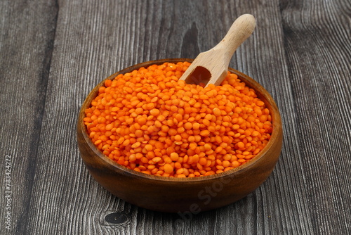 Red lentils in wooden bowl on wooden table background. Top view, copy space. Flat lay.
