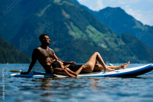 Sexy summer couple. Couple paddling in nature. Sensual fit sexy lovers on sup board paddle surfing. SUP surfing in summer vacation. Alps lake in Swiss. Couple in love on summer vacation in Switzerland