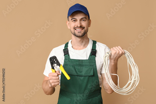 Portrait of male electrician with crimper and wires on beige background photo