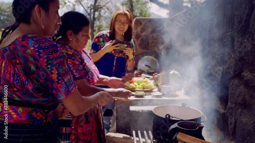 Two Latina women of the Mayan ethnic group cook and their daughter takes photos of them to share on social networks. photo