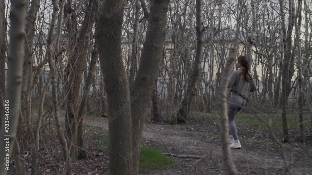 Pretty girl with brown hair wearing wireless headphones jogs through a nature park Pretty girl with brown hair wearing wireless headphones jogs through a nature park