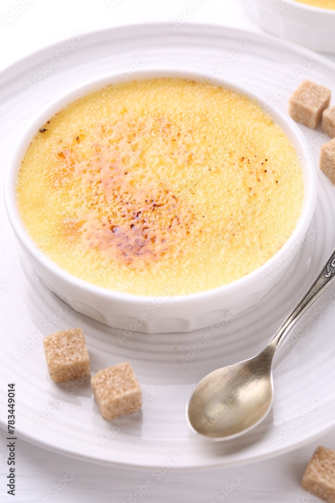 Delicious creme brulee in bowl, sugar cubes and spoon on white table Delicious creme brulee in bowl, sugar cubes and spoon on white table