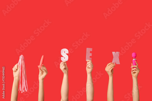 Female hands with sex toys against red background