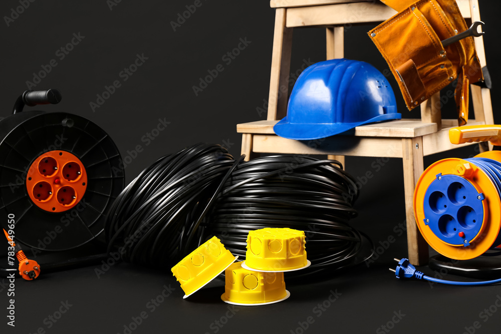 Obraz premium Stepladder with hardhat, rolled wires, extension cable reels and electrical junction boxes on black background