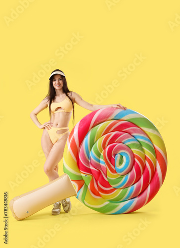 Pretty young woman in swimsuit with inflatable mattress in shape of candy on yellow background © Pixel-Shot