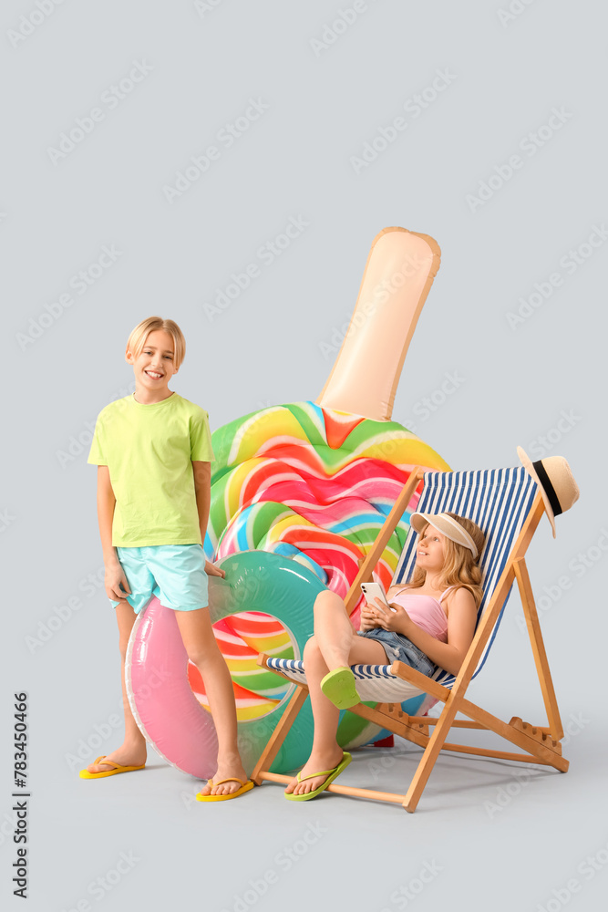 Cute little kids with inflatable ring, mattress and deckchair on grey background