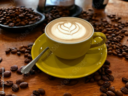 A latte in a yellow cup on a wooden table with coffee beans on the side.