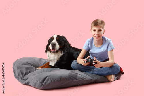 Little boy with Bernese mountain dog playing video game on pink background