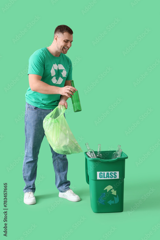 Male volunteer throwing glass bottles into recycle bin on green background Male volunteer throwing glass bottles into recycle bin on green background