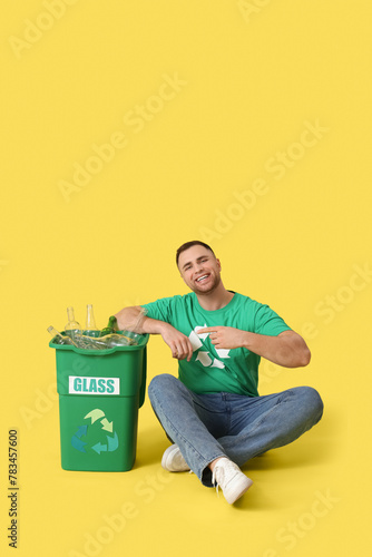 Male volunteer pointing at recycle bin with glass on yellow background