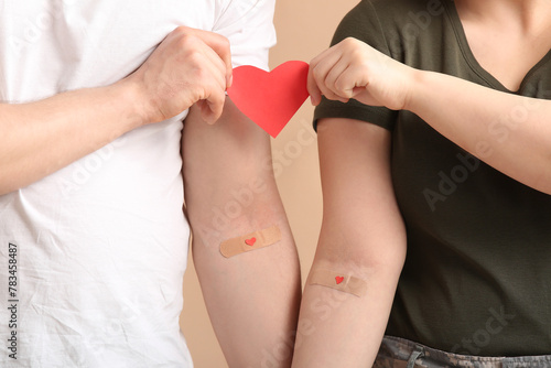 Blood donor and soldier with applied medical patches holding paper heart on beige background photo