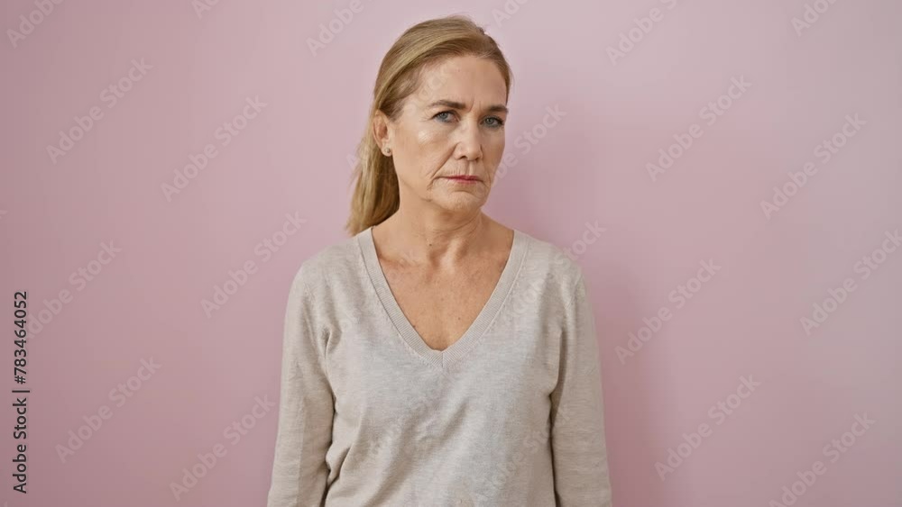 Blonde middle-aged woman nails a simple, natural look. stands with a serious expression, facing the camera over a pink isolated background Blonde middle-aged woman nails a simple, natural look. stands with a serious expression, facing the camera over a pink isolated background