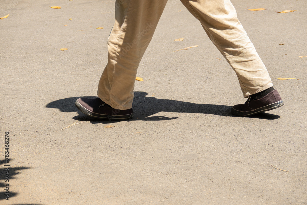 A man is walking on a sidewalk wearing brown shoes and tan pants
