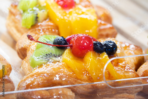 A tray of pastries with fruit on top. The fruit includes blueberries, cherries, and kiwi