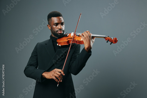 Elegant African American male musician in black suit playing violin against gray background, creating soulful melodies