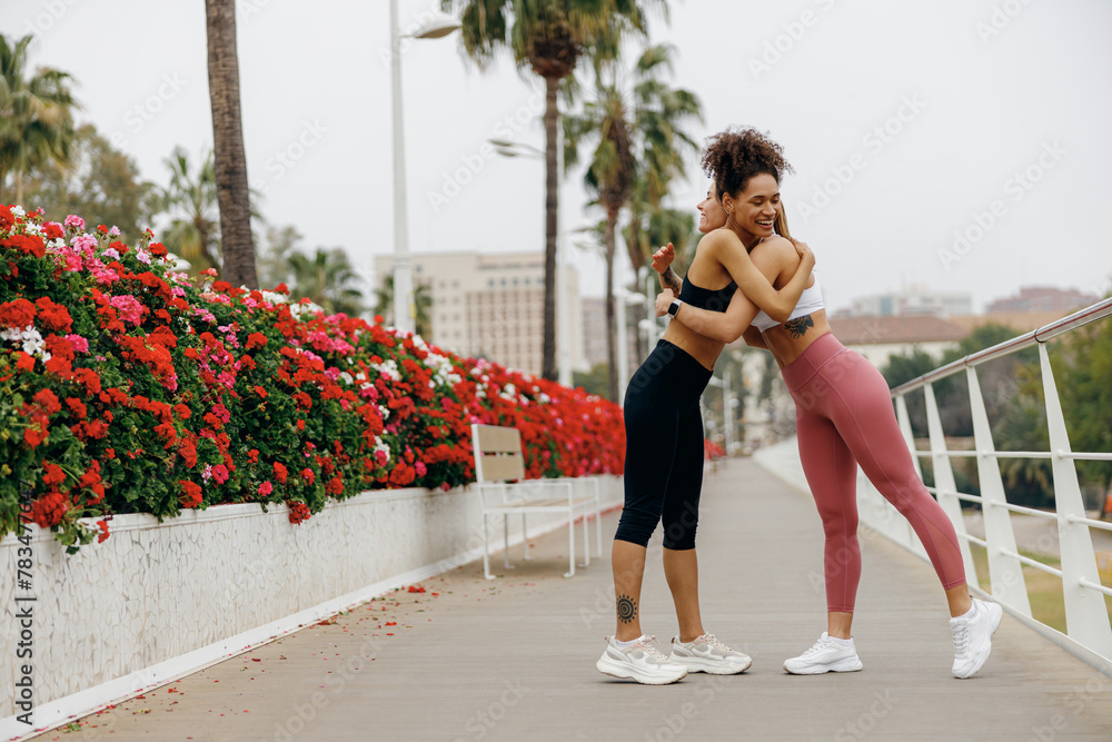 Obraz premium Young beautiful female friends in tracksuit hugging and smiling after outdoor training