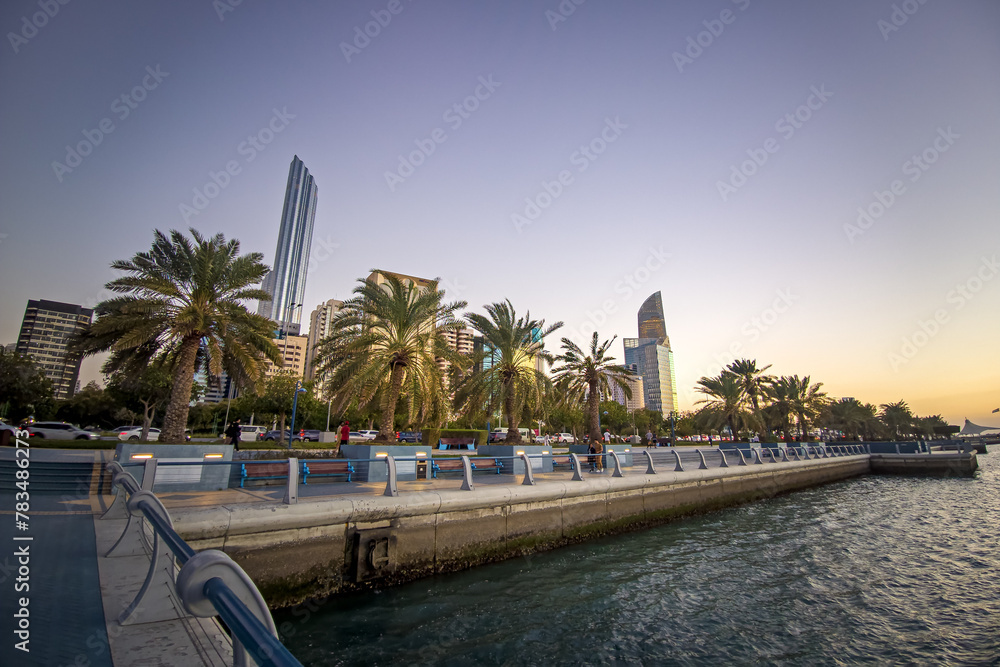 Strolling along the Abu Dhabi Corniche, a scenic waterfront promenade with stunning views of the Arabian Gulf and city's iconic skyscrapers - obrazy, fototapety, plakaty 