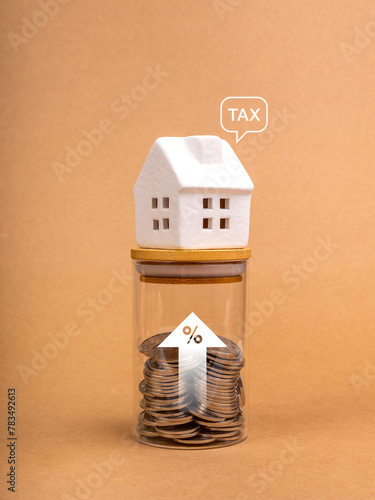 Home Tax, mortgage interest rates, property financial concept. Word "TAX" in speech bubble on white house on glass bottle with percentage icon and increasing arrow with coins inside, brown background.
