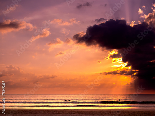 Fantastic background of gradient color sunset sky with beautiful sun rays behind dark cloud over the sea water. Summer sand beach scenery in evening time. Early morning sunrise or dusk seascape scene.