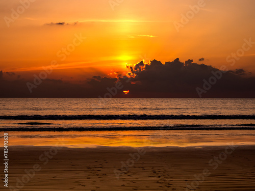 Beautiful background of sunset sky with sun rays behind black cloud over the sea water. Dark landscape and ocean scene. Summer sand beach in evening time. Early morning sunrise or dusk seascape.