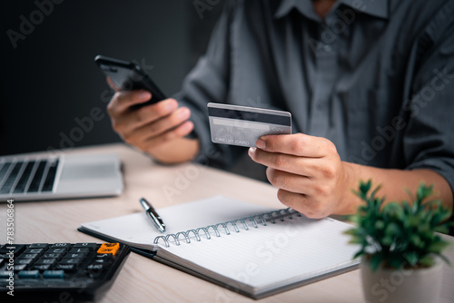 Man with credit card and smartphone finalizes a transaction, with a calculator and notepad nearby. online payment transaction e commerce shopping internet finance banking business concept. photo