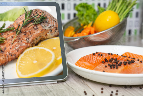 Fresh salmon fish with pepper and fresh vegetable preparing to cooking. Use digital tablet to search for cooking recipes. wireless technology.