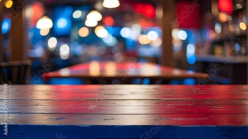 composition with a blurred bar background embellished with red bokeh lights and an empty blue hardwood tables that stands out. Dreamy atmosphere with magical blue bokeh and sparkling lights on a dark 