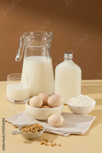 Brown and beige tone with a set of ingredient baking, a unlabeled glass bottle of soy milk beside many other ingredients such as eggs, flour, soybean. Photo with blank space 