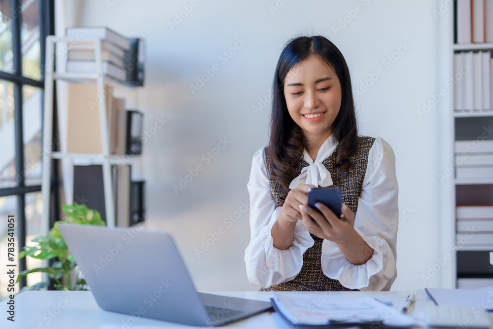 Content young asian businesswoman using smartphone at desk with laptop. Modern office technology and communication concept Content young asian businesswoman using smartphone at desk with laptop. Modern office technology and communication concept