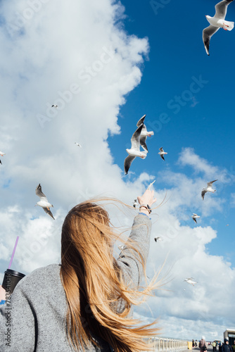 Young woman feeds seagulls. Сoastline scene with girl. Concept of travel (ID: 783541046)