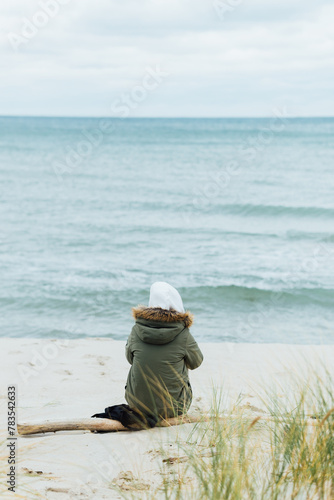 Girl sits on the beach, dreams and looks at the sea. Rear view, against the backdrop of the sea and waves