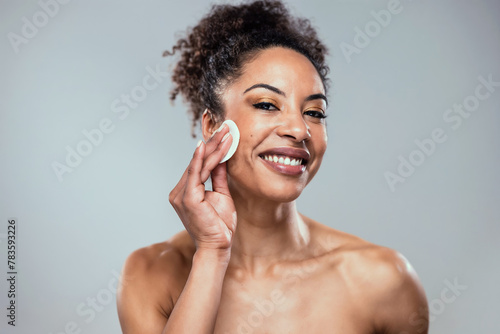 Beautiful woman removing makeup while taking care of her skin while looking at camera on isolated background