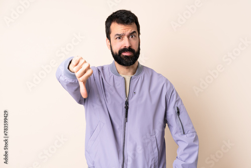 Caucasian man with beard wearing a jacket over isolated background showing thumb down with negative expression