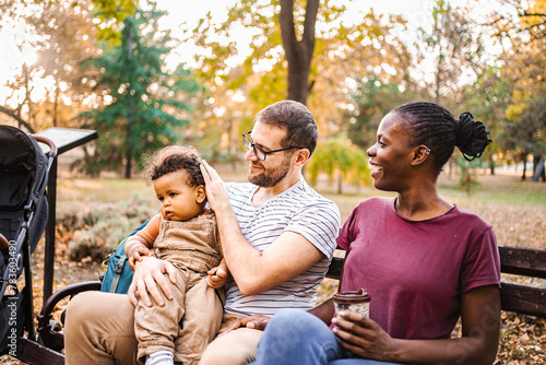 Mixed race couple is sitting on a park bench with their son