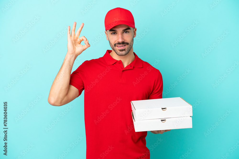 Delivery caucasian man picking up pizza boxes isolated on blue background showing ok sign with fingers Delivery caucasian man picking up pizza boxes isolated on blue background showing ok sign with fingers