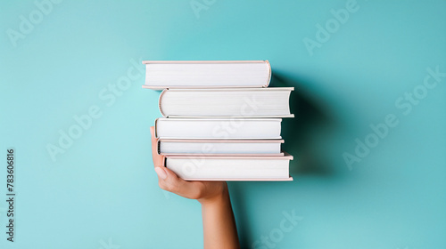 Empilement de livres , une main de femme tenant par dessous une pile de livres nouveaux sur fond bleu clair. Éducation, bibliothèque, science, connaissances, études, échange de livres, passe-temps