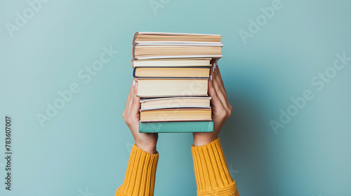 Empilement de livres , mains de femme tenant par dessous une pile de livres nouveaux sur fond bleu clair. Éducation, bibliothèque, science, connaissances, études, échange de livres, passe-temps