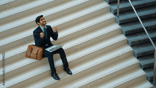 Top view business man celebrate successful project while sitting at stairs. Smart project manager getting new gob, getting promotion, increasing sales while calling friends by using laptop. Exultant. photo