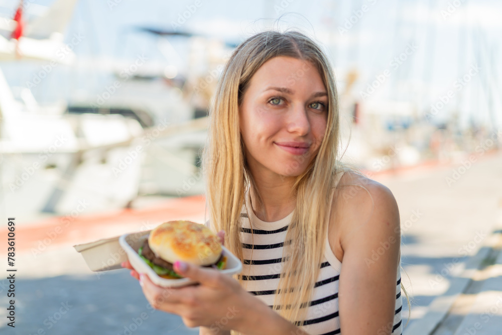 Young blonde woman at outdoors holding a burger Young blonde woman at outdoors holding a burger