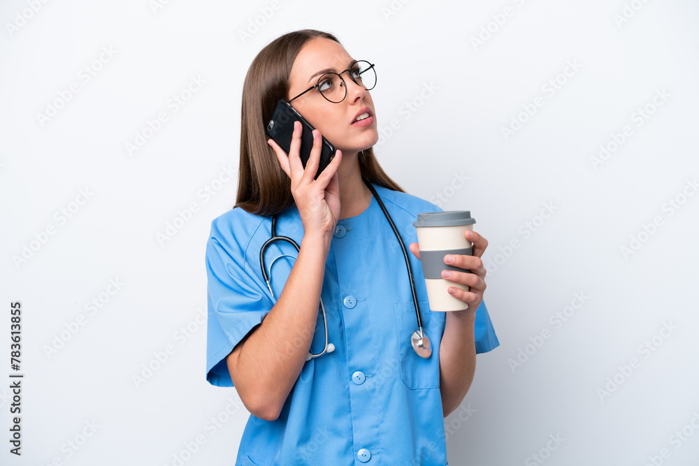 Young nurse caucasian woman isolated on white background holding coffee to take away and a mobile Young nurse caucasian woman isolated on white background holding coffee to take away and a mobile