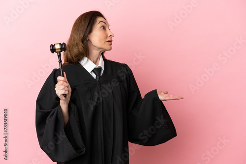 Middle aged judge woman isolated on pink background with surprise expression while looking side photo